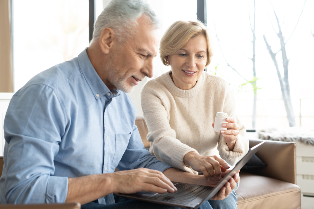 Senior couple with pills and laptop in living room